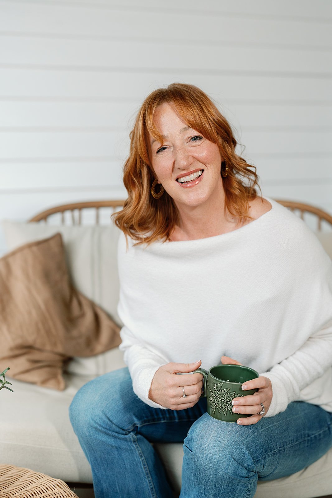 Amanda Alexander standing with arms crossed, wearing an oatmeal v-neck jumper